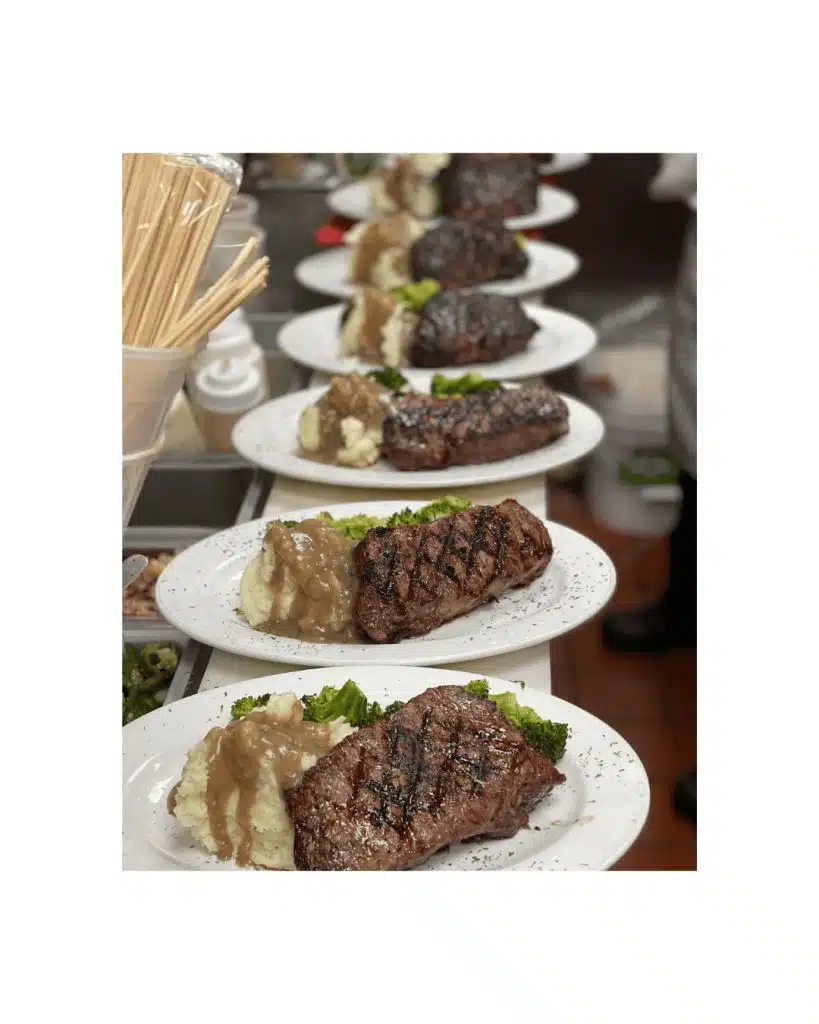 A line of grilled NY strip steaks served with mashed potatoes, gravy, and steamed broccoli at NY Firehouse Grille
